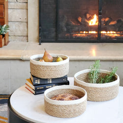 Rustic woven baskets with fruits and herbs on a table, cozy fireplace background.