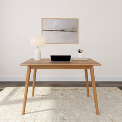 Minimalist home office setup with wooden desk, laptop, desk lamp, and art piece.