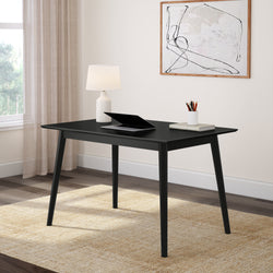Minimalist black desk in modern home office with laptop, lamp, and wall art.