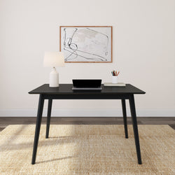 Modern minimalist home office setup with black desk, laptop, lamp, and abstract wall art.