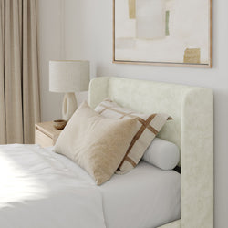 Elegant bedroom interior with modern beige decor, stylish pillows, and cozy bedside lamp.
