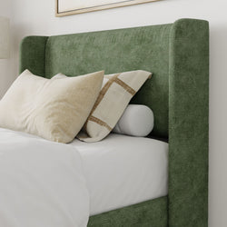 Green upholstered bed with beige and white pillows in a modern bedroom setting.
