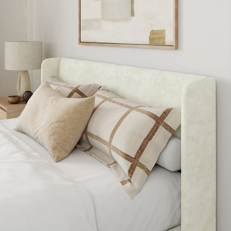 Modern bedroom with an elegant beige upholstered bedframe, stylish throw pillows, and a contemporary nightstand with a decorative lamp.