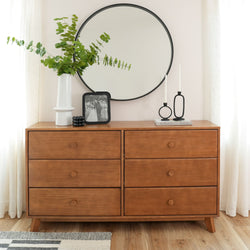 Mid-century modern wooden dresser with round mirror, decorative vase, and candlesticks for stylish bedroom decor.