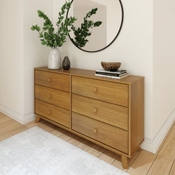 Modern wooden dresser with six drawers, adorned with decor and a round mirror, in a stylish bedroom corner.
