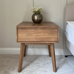 Mid-century modern wooden bedside table with a single drawer and a vase of white flowers placed on top.