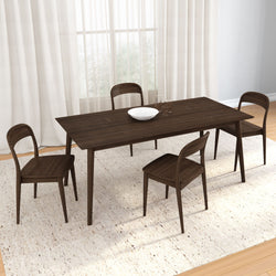 Mid-century modern dark walnut 4-person dining table and chairs on a light textured rug with a white bowl and glasses in a bright room with sheer curtains
