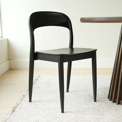 Black wooden dining chair with curved backrest and tapered legs beside wooden dining table on neutral rug in minimalist modern dining room