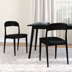 Pair of minimalist black dining chairs with curved backs and a rectangular black dining table topped with a white bowl and glass, set on a light textured rug by sheer curtains