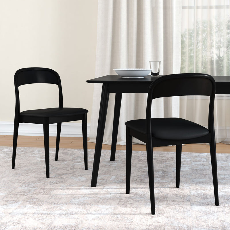 Pair of minimalist black dining chairs with curved backs and a rectangular black dining table topped with a white bowl and glass, set on a light textured rug by sheer curtains