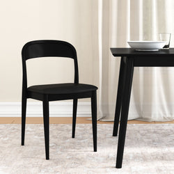 Black modern dining chair beside black dining table with white bowl and glass in a minimalist dining room with sheer curtains, hardwood floor and neutral area rug