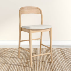 Natural wood bar stool with white cushion on a textured beige rug.