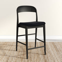 Modern black barstool with sleek design on a textured beige rug in a minimalist room setting.