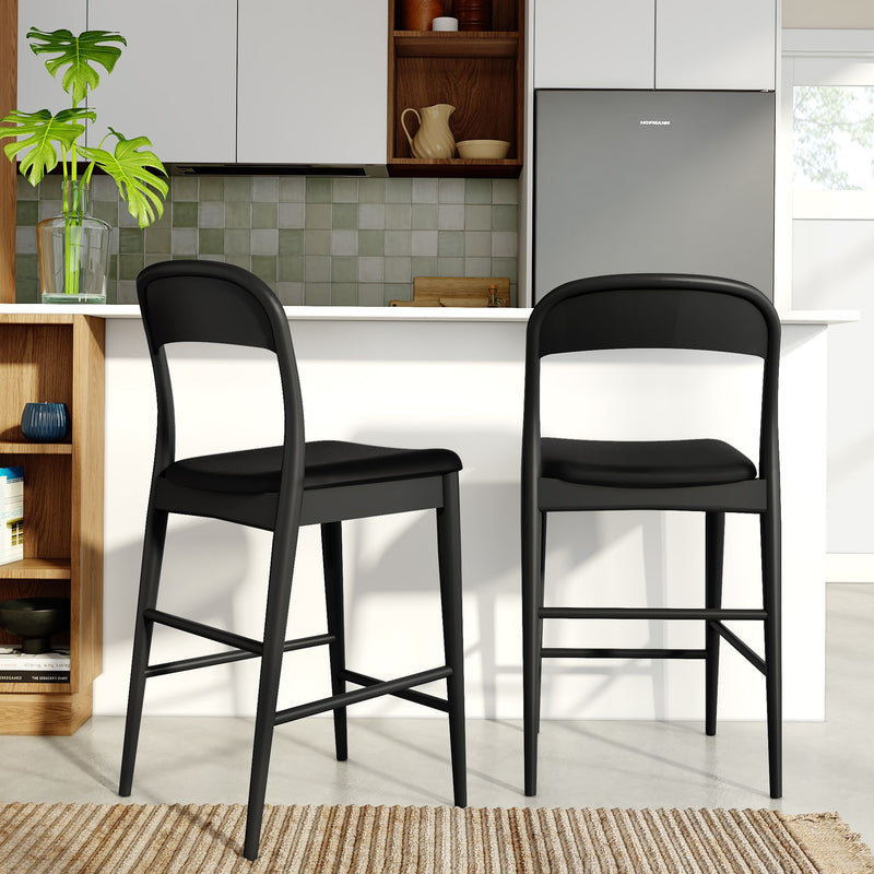 Two black modern bar stools with padded seats at a white kitchen island in a contemporary kitchen with green tile backsplash, stainless-steel refrigerator and potted monstera plant.