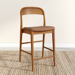 Mid-century modern wooden counter stool with curved back and brown leather seat on natural woven jute rug