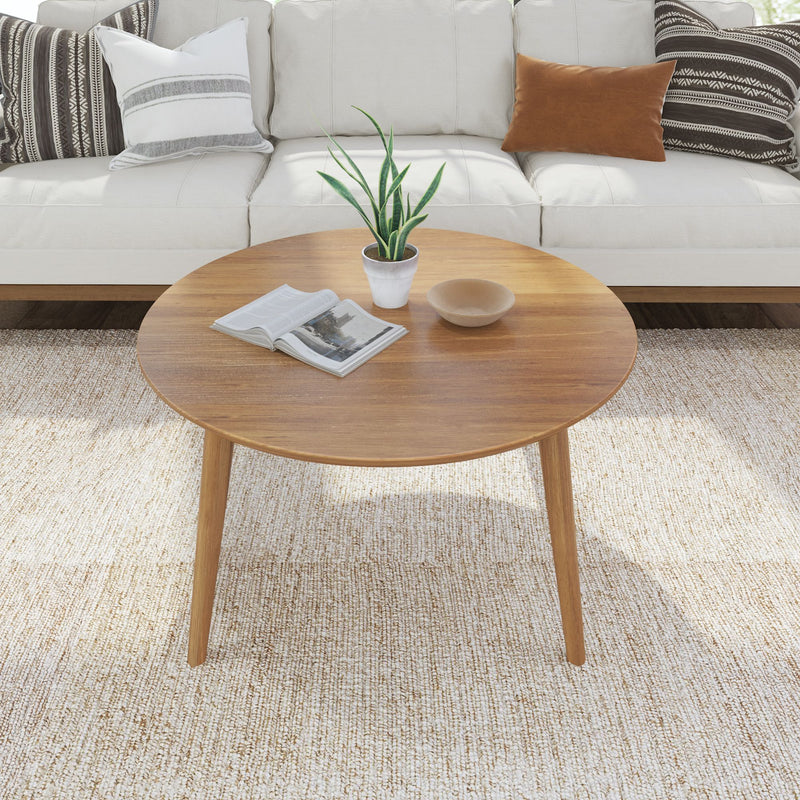 Round wooden coffee table with plant, book, and decor in a modern living room setting.