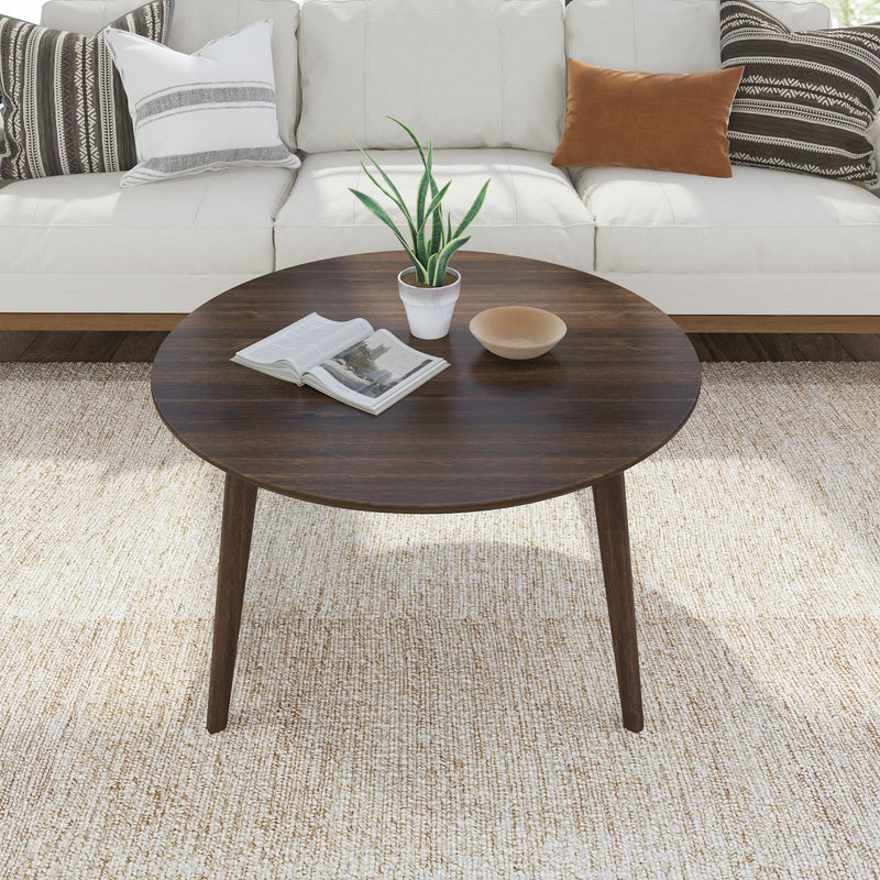 Round wooden coffee table with plant and book, set in modern living room with beige couch and decorative pillows.