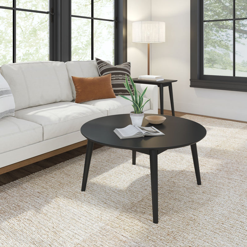 Modern living room with white sofa, black round coffee table, indoor plant, and natural light through large windows.