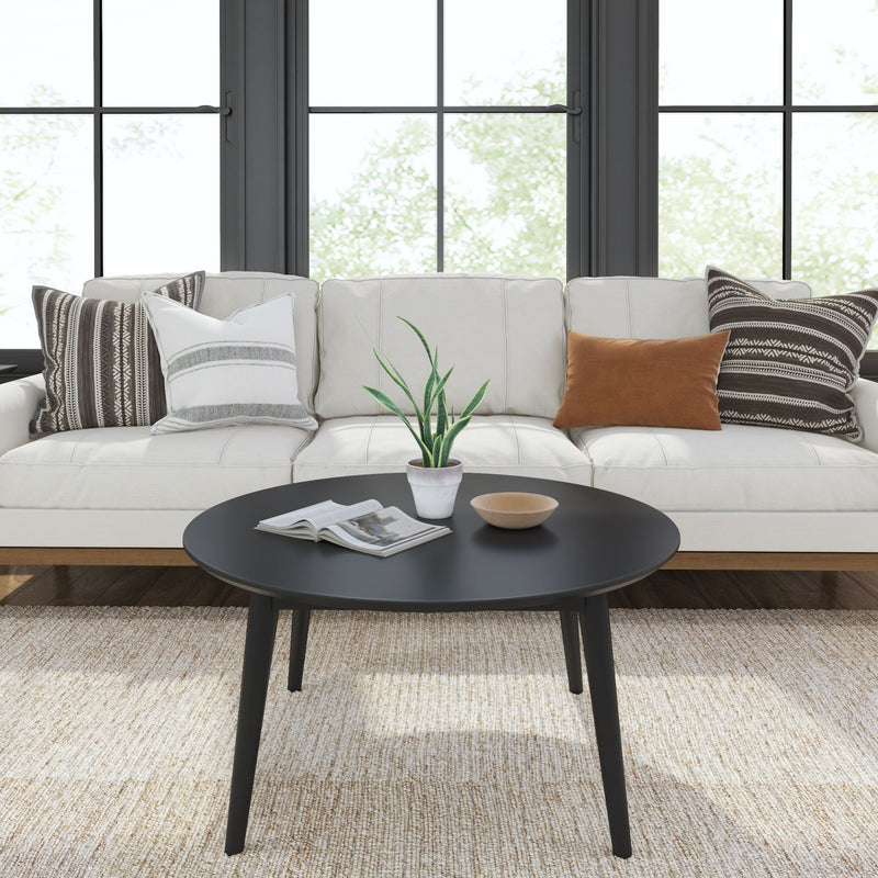 Modern living room with white sofa and decorative pillows, featuring a sleek black coffee table with a plant and book, against large windows.