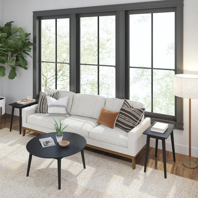 Modern living room with white sofa, decorative pillows, black coffee table, large windows, and indoor plant.