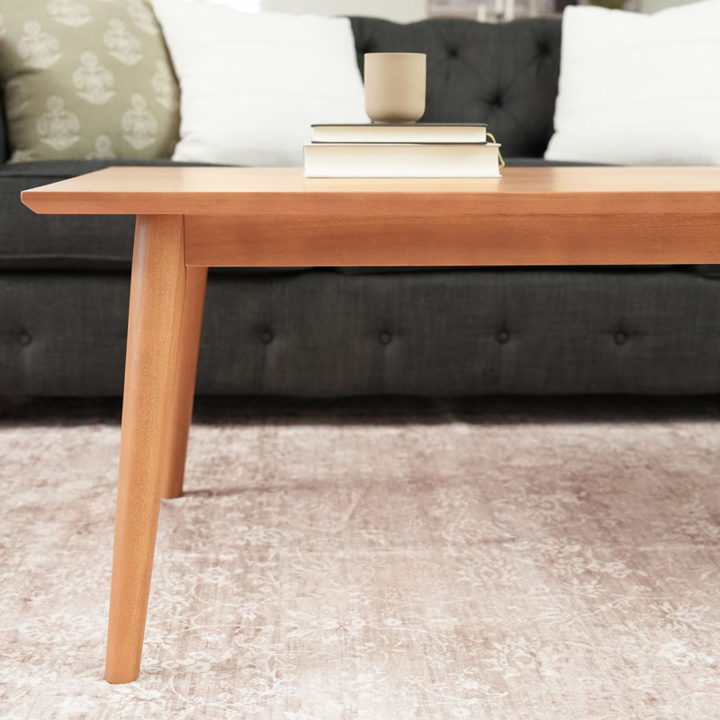 Modern wooden coffee table with books and a cup, in front of a dark gray sofa in a stylish living room setting.