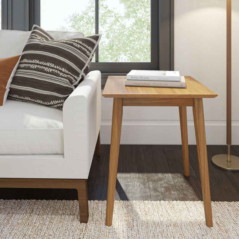 Mid-century modern wooden side table next to a white sofa with a patterned pillow, featuring natural light filtering through a window.