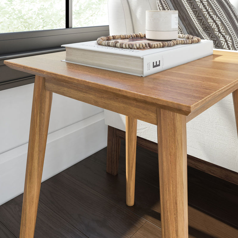 Mid-century modern wooden side table with a decorative book, candle, and beads, placed on dark hardwood flooring near a window.
