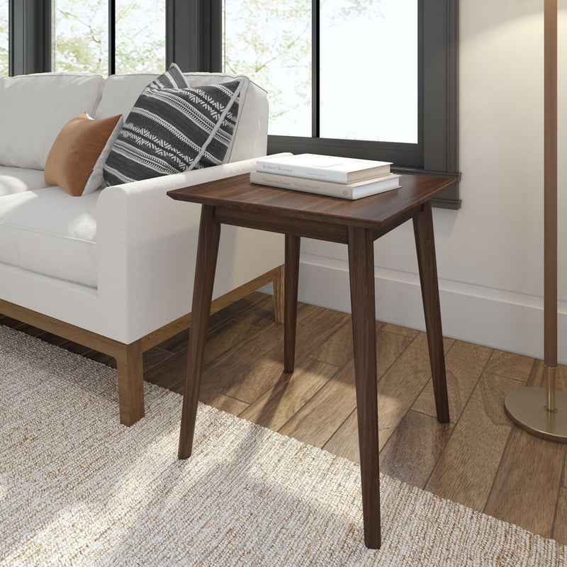 Modern wooden side table next to white sofa with decorative pillows in a bright living room.