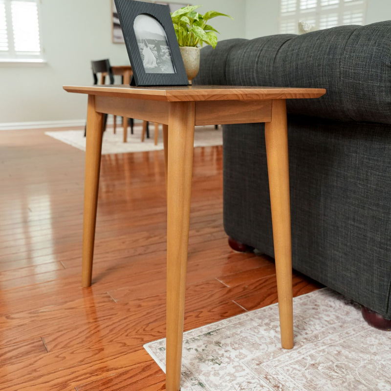 Mid-century modern wooden side table next to a gray sofa in a living room with hardwood flooring and a decorative rug.