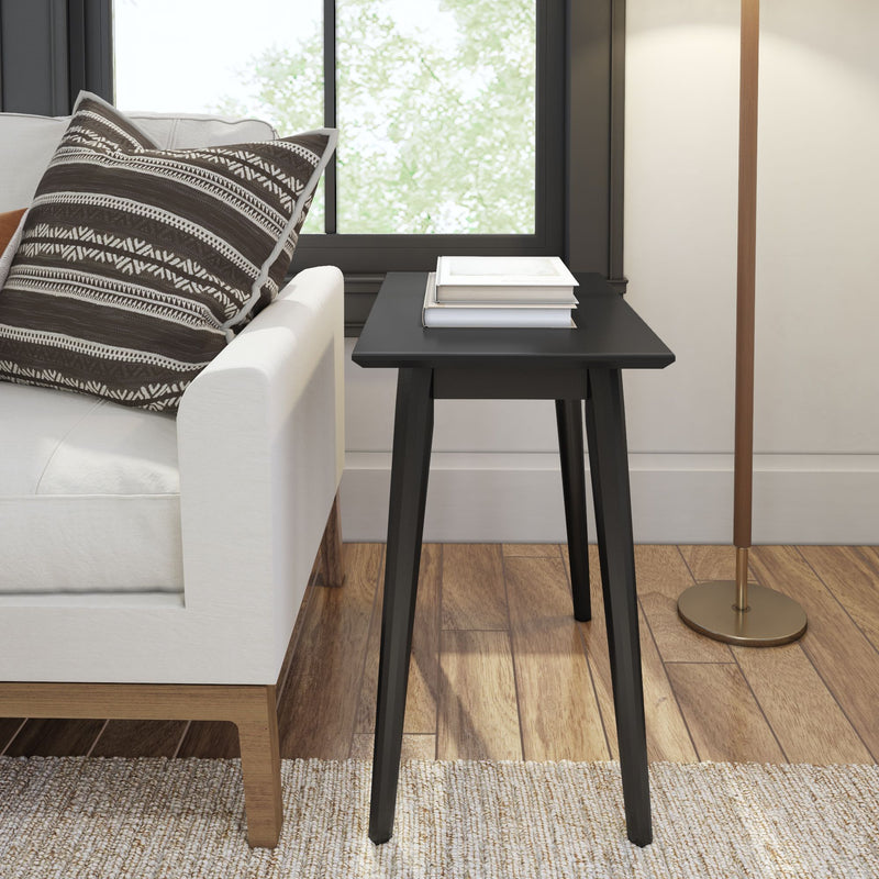 Black modern side table in a stylish living room setup with a white sofa and patterned pillow.