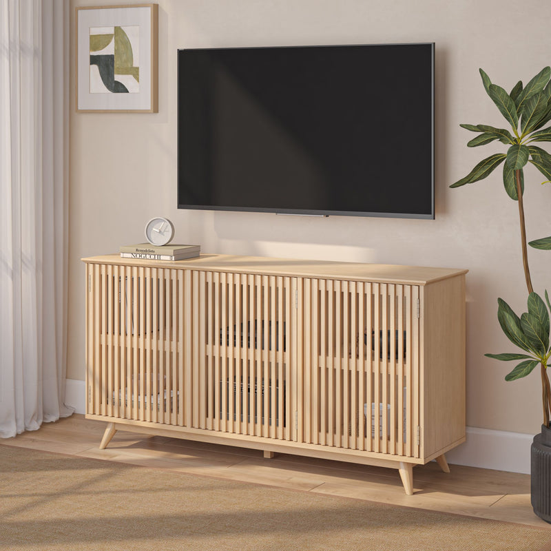Minimalist Scandinavian light oak slatted media console TV stand with storage and mid-century tapered legs beneath a wall-mounted flat-screen TV in a neutral living room featuring framed abstract art, tabletop clock and potted plant