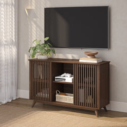 Mid-century modern dark walnut slatted-door TV console and wood media cabinet in bright living room with wall-mounted flat-screen TV, potted plant, books, game console and woven basket
