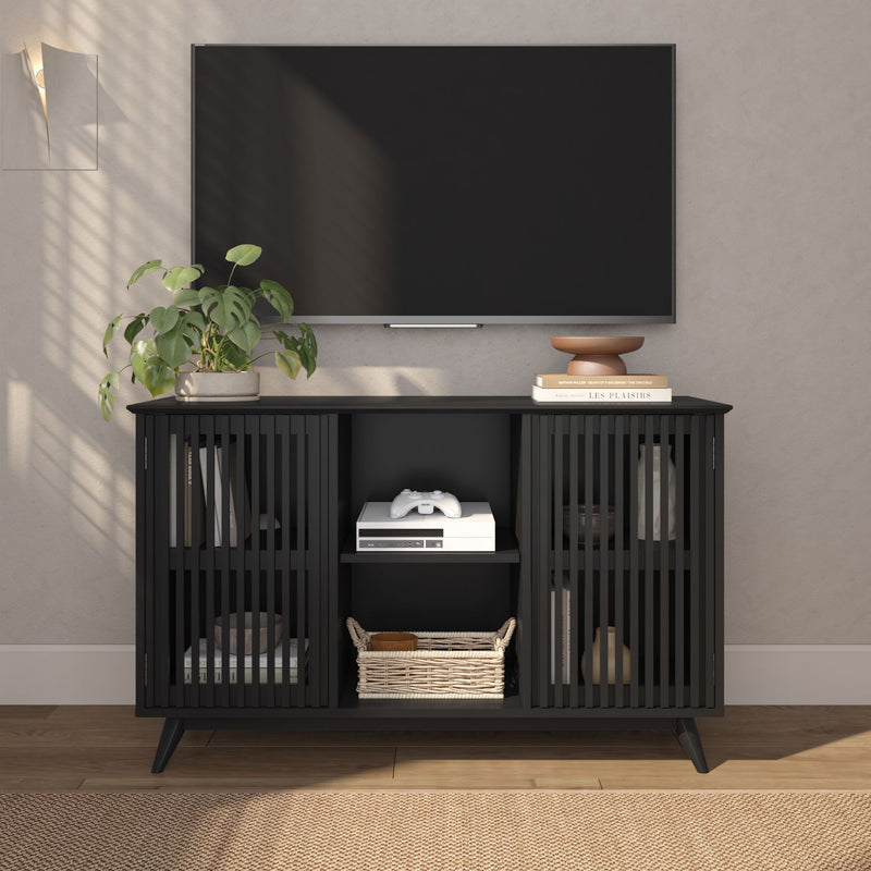 Wall-mounted flat-screen TV above a black slatted media console with potted plant, books, game console and wicker basket in a modern neutral living room.