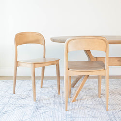 Light wood modern dining chairs and round table on a textured area rug in a minimalist Scandinavian dining room