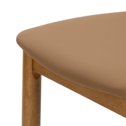 Close-up of tan leather dining chair seat showing textured upholstery and oak wood frame — mid-century modern chair detail