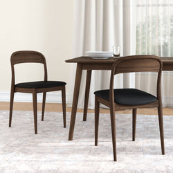 Mid-century modern walnut dining set with two wooden chairs featuring black upholstered seats around a compact rectangular table on a neutral area rug with sheer curtains and tableware