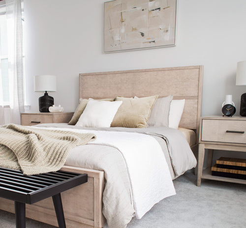 Modern cozy bedroom with beige bedding, wooden headboard, and abstract wall art.
