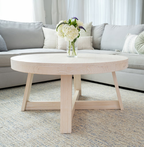 Round wooden coffee table with a floral centerpiece in a modern living room setting.