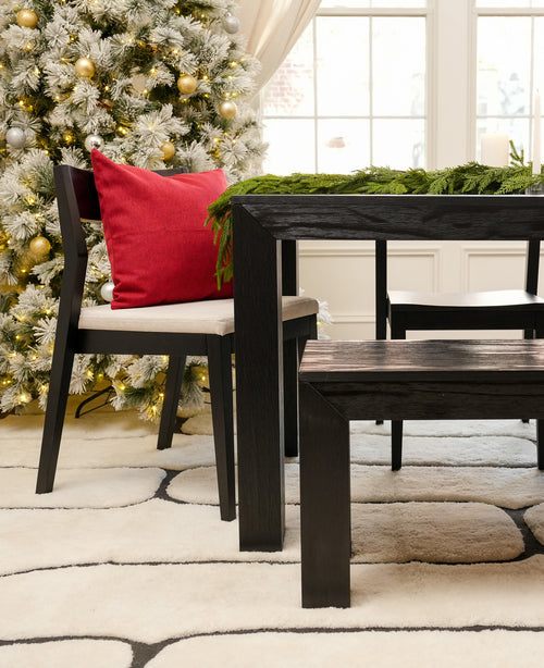 Modern dining room with a festive Christmas tree, red cushion, and dark wood table and bench.