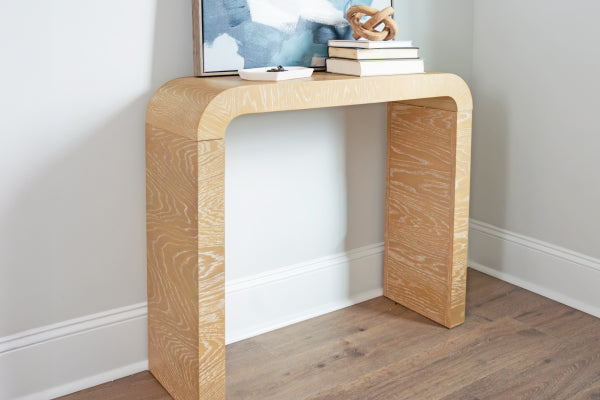 Minimalist light oak console table with rounded edges styled with books, abstract art, and a decorative knot on hardwood floor