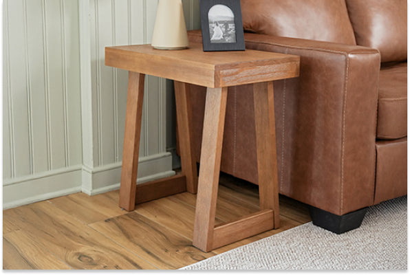 Solid wood rustic side table beside a brown leather sofa on hardwood flooring in a minimalist living room, styled with a small lamp and framed photo