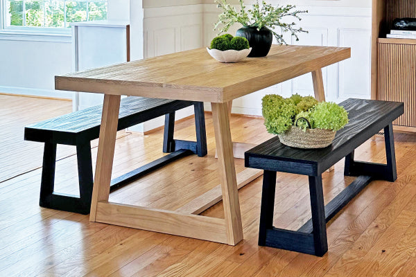 Modern farmhouse light wood dining table with two black wooden benches on hardwood floor, minimalist rustic dining set with green centerpiece and natural light