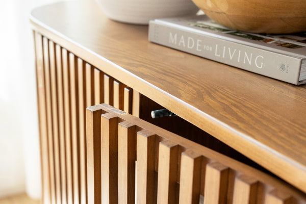 Close-up of mid-century modern light oak wooden sideboard with vertical slatted doors, decorative bowls and "Made for Living" book on top