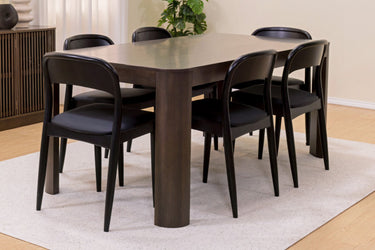 Dark wood rectangular dining table with six black mid-century modern chairs on a light beige rug in a bright contemporary dining room