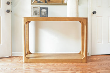 Mid-century modern light wood console table on hardwood floor in bright entryway with minimalist decor and framed photos
