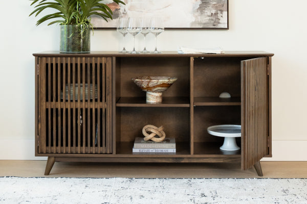 Mid-century modern wooden credenza with slatted doors, open shelves with a decorative bowl, books, plant and wine glasses.