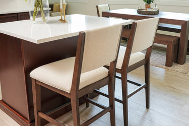 Contemporary kitchen island with white quartz countertop and two beige upholstered wooden bar stools on light hardwood floor