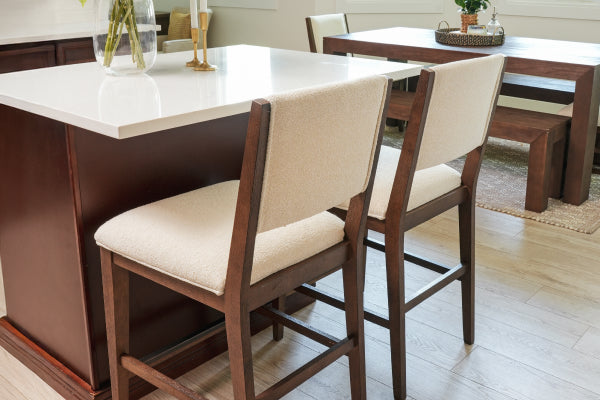 Contemporary kitchen island with white quartz countertop and two beige upholstered wooden bar stools on light hardwood floor