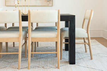 Modern dining room with black wood dining table, light wood upholstered chairs and textured neutral area rug in Scandinavian-style interior