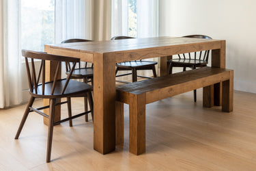 Light-filled modern farmhouse dining room with solid wood rectangular dining table, wooden bench, and spindle-back chairs on hardwood floor